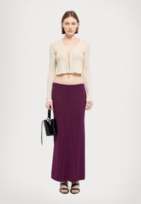 Cardigan bej cu împletitură, stil scurt, asortat cu o fustă lungă violet. Un rucsac negru și sandale plate completează ținuta.