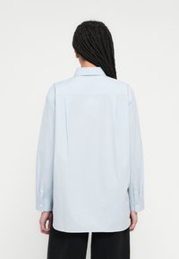 Gaiši zila, garroku krekls ar smailu apkakli, pogu aprocēm un taisnu griezumu, ar muguras yoke un gludu tekstūru.