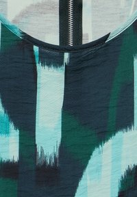 Tessuto multicolore con motivi astratti di pennellate in turchese, verde scuro e nero. Texture liscia con scollatura rotonda e dettaglio con zipper.