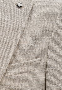 Hellgraue strukturierte Stoffjacke mit einem glatten schwarzen Knopf, ausgestattet mit einer Brusttasche und feinen gewebten Details in einem zeitgenössischen Design.