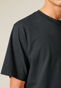 T-shirt en coton noir avec un col rond et des manches courtes. Présente une texture lisse et une coupe régulière. Design simple sans motifs ni embellissements.