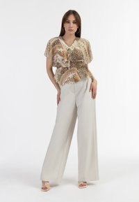 Lett, svævende bluse i beige med intrikate mønstre og leopardprint; parret med højtsiddende, vide cremede bukser.