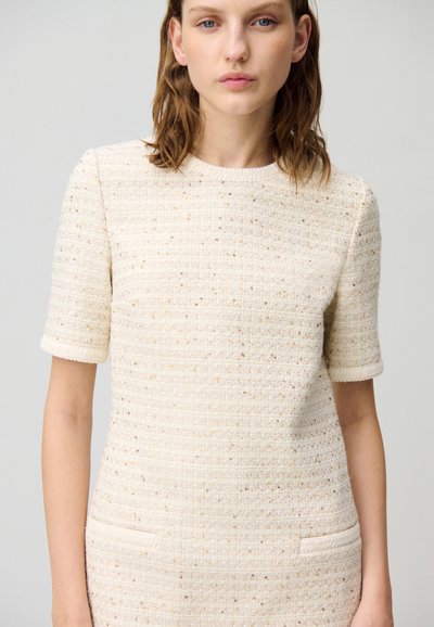 Robe en tweed crème à manches courtes, col rond et deux poches latérales. Présente un motif texturé avec des fils métalliques subtils.