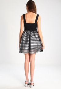 Svart ärmlös topp med breda axelremmar, i kombination med en veckad silverfärgad metallickjol med horisontella ränder.