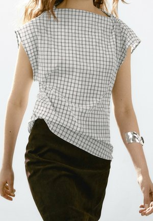 Woman wearing white and gray checkered sleeveless top with squared neckline, black skirt, and silver cuff bracelet on right wrist.
