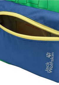 Sac Jack Wolfskin bleu et vert avec une fermeture éclair jaune partiellement ouverte dévoilant un livre à l'intérieur intitulé "Born to Be Child".