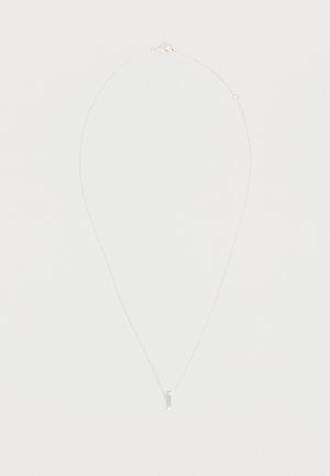 Collier délicat en chaîne argent avec un petit pendentif croix verticale sur un fond clair.