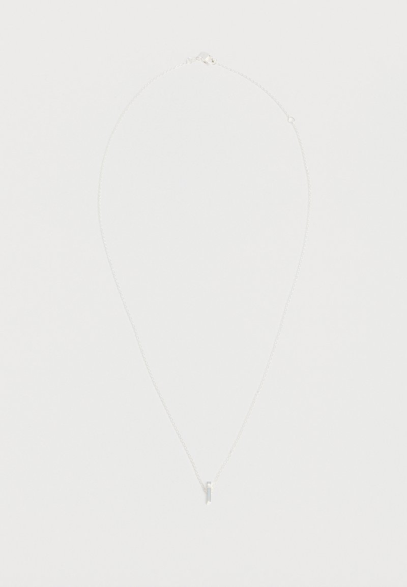 Collier délicat en chaîne argent avec un petit pendentif croix verticale sur un fond clair.