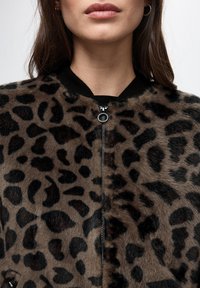 Leopard print faux fur bomber jacket featuring a black ribbed collar, a zip front, and soft texture. Notable for its distinctive pattern.