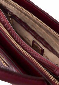 Wnętrze bordowej skórzanej torebki z beżową podszewką, wyposażone w wiele przegródek i kieszeni na zamek. Akcenty w kolorze złotym.