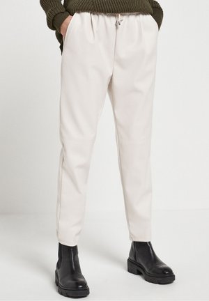 Unterkörper mit cremeweißer Hose mit elastischem Bund und Kordelzug, kombiniert mit schwarzen klobigen Stiefeletten und einem dunkelgrünen Pullover.