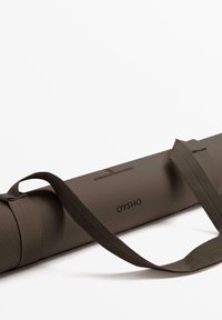 Barna jóga mat tasak, textúrált felülettel, állitható szovet pántokkal és logoval, ami az oldalára van gravirozva. Henger alakú dizájnja megkönnyíti a szállítást.