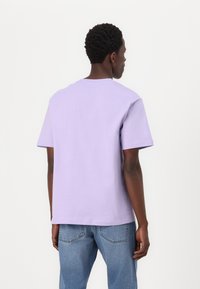 Camiseta de manga corta en color lila, hecha de tejido de algodón y con un corte relajado. Cuenta con un cuello redondo y la parte trasera lisa, combinada con vaqueros azules.