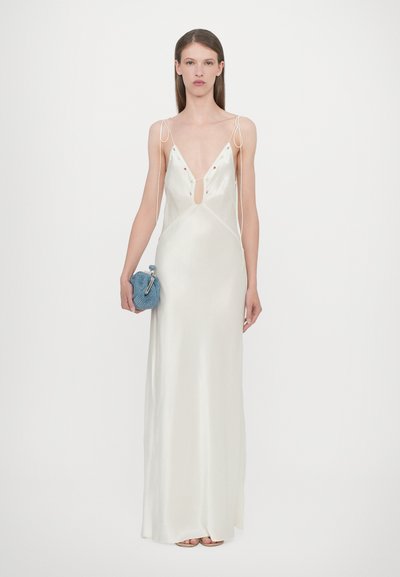 Satin slip dress in ivoor met een diepe V-halslijn, verstelbare spaghettibandjes en bloemversieringen. Model houdt een blauwe clutch vast.