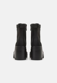 Czarne botki do kostki o gładkiej fakturze, z zamkiem błyskawicznym i masywniejszym obcasem z tłoczonym logo po boku. Minimalistyczny i nowoczesny design.