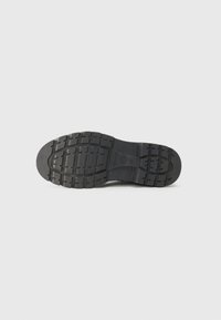 Semelle de chaussure en caoutchouc noir avec motif de semelle texturé, présentant des rainures pour une meilleure traction et stabilité. Design plat, sans accents notables.