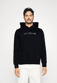 Black hooded sweatshirt with front pocket, featuring embroidered "HILFIGER" logo in multicolored letters. Soft texture and casual fit.