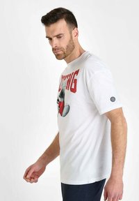 Camiseta blanca de manga corta con un gran estampado gráfico de un guante de boxeo y la palabra "BOXING" en rojo. Incluye un logo circular en la manga.