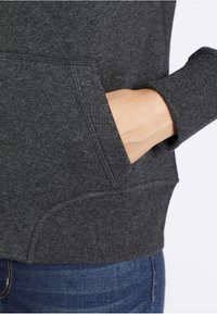 Sudadera color gris carbón con tejido texturizado, que incluye un bolsillo frontal y mangas con puños. Presenta un detalle de costura lateral con un ajuste holgado.