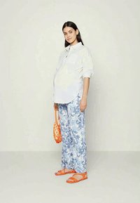 Camisa branca de botão, calças azuis com padrão floral, sandálias laranjas e uma bolsa de malha laranja. Foco em tecidos leves e ajuste descontraído.