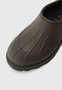 Barna gumi slip-on cipő bordázott textúrával, sima orr résszel és fekete talppal. Nincs látható fűzés vagy hardver.