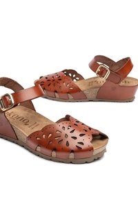 Brown leather sandals with cut-out floral design, adjustable ankle strap, cork footbed, and a textured rubber sole.