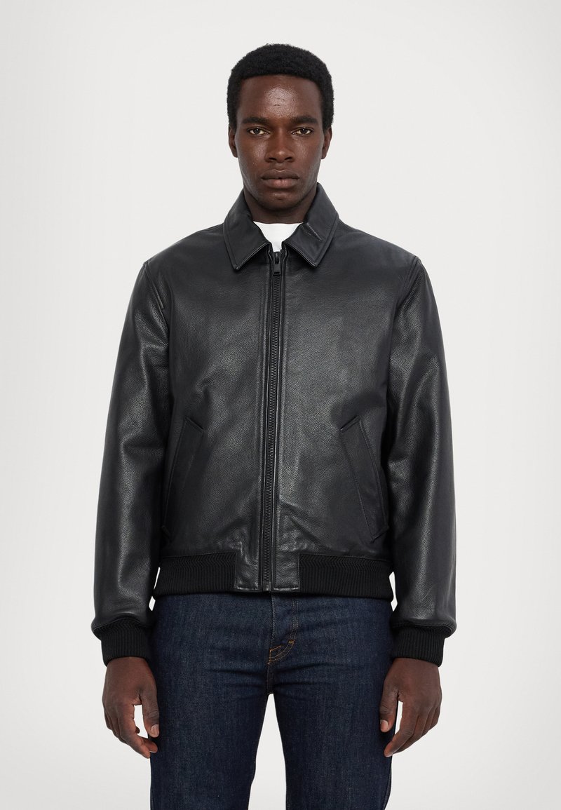Chaqueta de cuero negro con cierre de cremallera, puños y dobladillo acanalados, y un cuello clásico. Cuenta con bolsillos laterales y una textura suave.