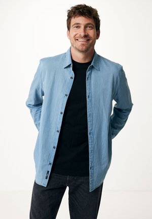 Lichtblauw overhemd met knopen in zachte stof, met een puntkraag, twee borstzakken en bruine knopen, gedragen over een zwart T-shirt.