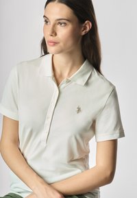 Polo shirt light cream con maniche corte, tre bottoni e un piccolo logo ricamato sul petto. Tessuto di cotone morbido e colletto classico.