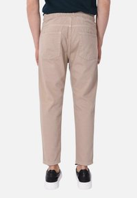 Pantaloni beige con elastico in vita, due tasche posteriori e gamba affusolata. Indossati con scarpe nere.