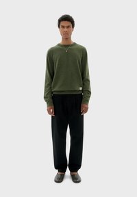 Zelený pletený svetr s kulatým výstřihem, který je spárován s černými volnými kalhotami a šedými botami na slip-on. Minimalistický design s běžným střihem.
