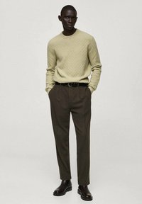 Pull en tricot vert clair avec un motif texturé, associé à un pantalon brun foncé. Le modèle porte une ceinture noire et des bottines.