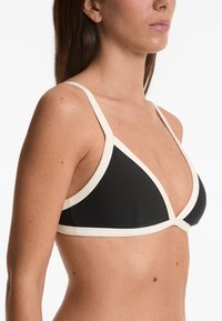 Fekete bikini felső krémszínű díszítéssel, háromszög alakú kialakítással és állítható pántokkal. Simább textúrával és minimalista stílussal rendelkezik.