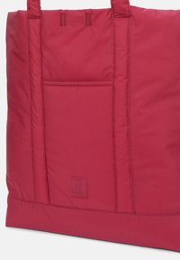 Borsa tote in nylon rossa con tasca frontale, dettagli cuciti e patch del logo Timberland nell'angolo in basso a destra. Tessuto morbido, forma rettangolare.