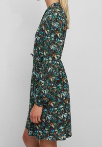 Vestido floral con un fondo marrón oscuro y patrones en verde, azul y naranja, mangas largas, cintura ajustada y falda acampanada.