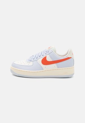 Tenisky Nike Air Force 1 mají bílou koženou svršek s světle modrými akcenty, oranžovým logem Nike a krémovou podešví.