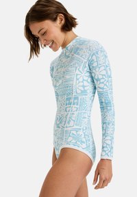 Dlouhý rukáv bodysuit v světle modré barvě s bílými tropickými vzory. Má přiléhavý střih, vysoký límec a hladkou, elastickou látku.