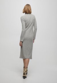 Robe en tricot ribbed grise à manches longues, longueur genou, présentant une silhouette cintrée et un col rond. Portée avec des bottines métalliques dorées.