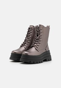 Botas de tobillo en gris metálico con suela gruesa negra, cordones en la parte delantera y una lengüeta, fabricadas con un material sintético suave y un acabado texturizado.