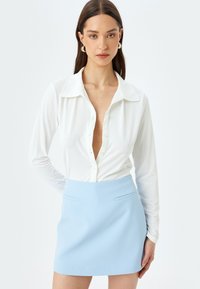 Witte lange mouw blouse met een diepe V-hals en knopen, gecombineerd met een lichtblauwe minirok met twee voorzakken.
