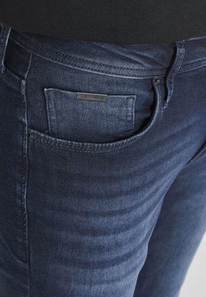 Dunkelblaue Denim-Jeans mit sichtbaren Nähten und einer kleinen Vordertasche mit einem Metall-Logoetikett.