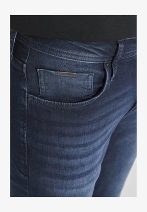 Dunkelblaue Denim-Jeans mit sichtbaren Nähten und einer kleinen Vordertasche mit einem Metall-Logoetikett.