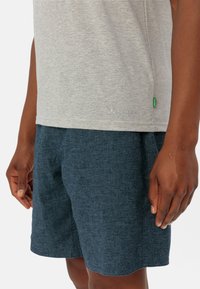 Camicia grigia a righe con maniche corte abbinata a pantaloni corti texturizzati blu scuro. Presenta un dettaglio del logo sulla camicia e un'etichetta verde.