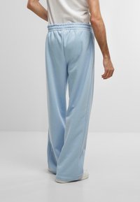 Light blue, wide-leg sweatpants with an elastic waistband, soft texture, and side seams visible, paired with white sneakers.