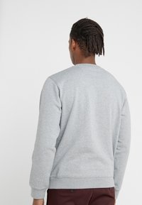 Sudadera gris con cuello redondo, tela texturizada, puños y dobladillo acanalados. La parte trasera presenta un acabado liso y no tiene logotipos visibles ni decoraciones.