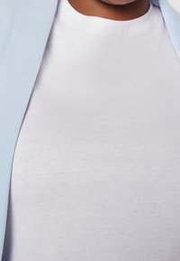 Close-up of a person wearing a white crew-neck shirt and a light blue blazer, showing neck and upper chest area.