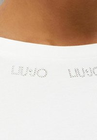 Hvid kortærmet t-shirt med "LIU JO" tekst i gnistrende rhinsten over halsudskæringen, lavet af blødt og glat bomuldsstof.
