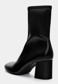 Bottine noire à design épuré, en cuir lisse. Dotée d'un talon bloc et de coutures invisibles sur le bord supérieur.