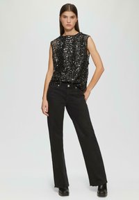 Schwarzes ärmelloses Oberteil mit Paillettenverzierungen, kombiniert mit hochtaillierten schwarzen Jeans. Die Jeans haben einen leicht ausgefransten Saum und einen geraden Schnitt.