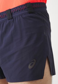 Marinefarbene Sportshorts aus leichtem Material, mit einem strukturierten Muster, seitlichen Schlitzen und einem schwarzen elastischen Bund mit Akzentdetails.